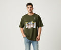 Man wearing olive green oversized t-shirt with anime graphic print on front, casual streetwear style on plain background
