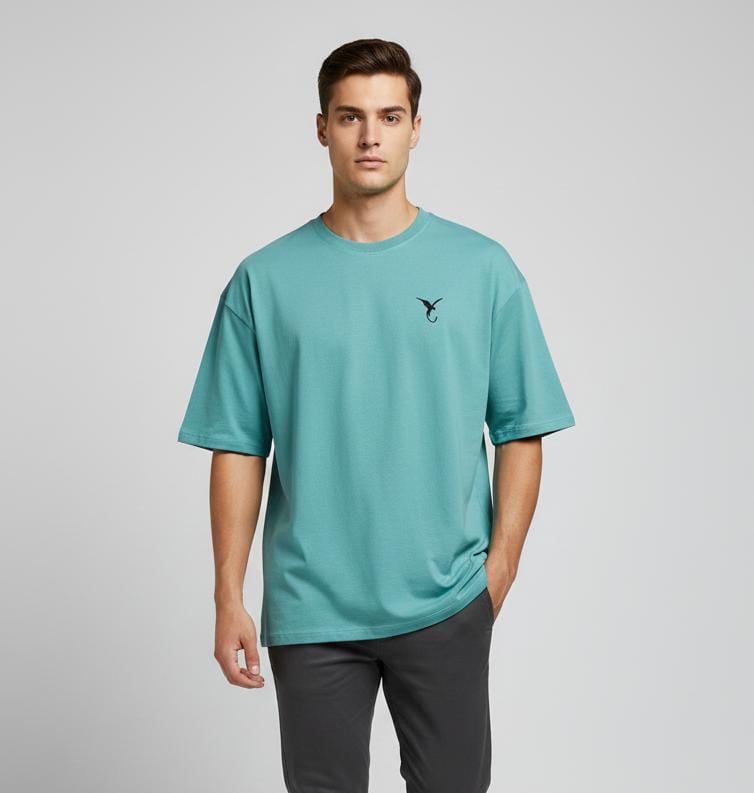Man wearing teal blue oversized men’s t-shirt with minimal chest logo, short sleeves, casual fit on plain background
